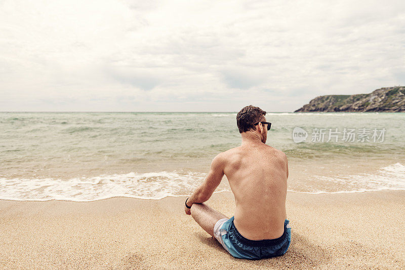 一个年轻人坐在康沃尔的Pedn Vounder海滩岸边